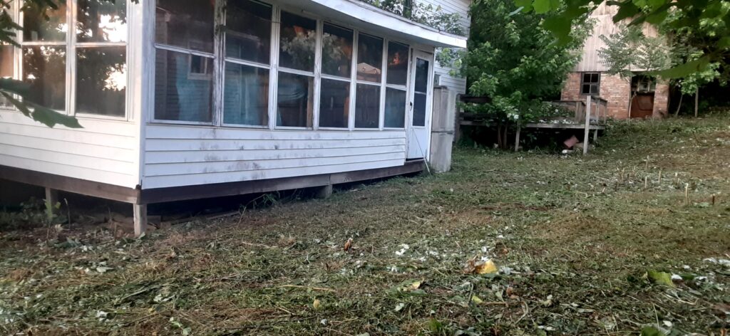 Before photo of white two-story house with red door and unkempt lawn before exterior renovation

