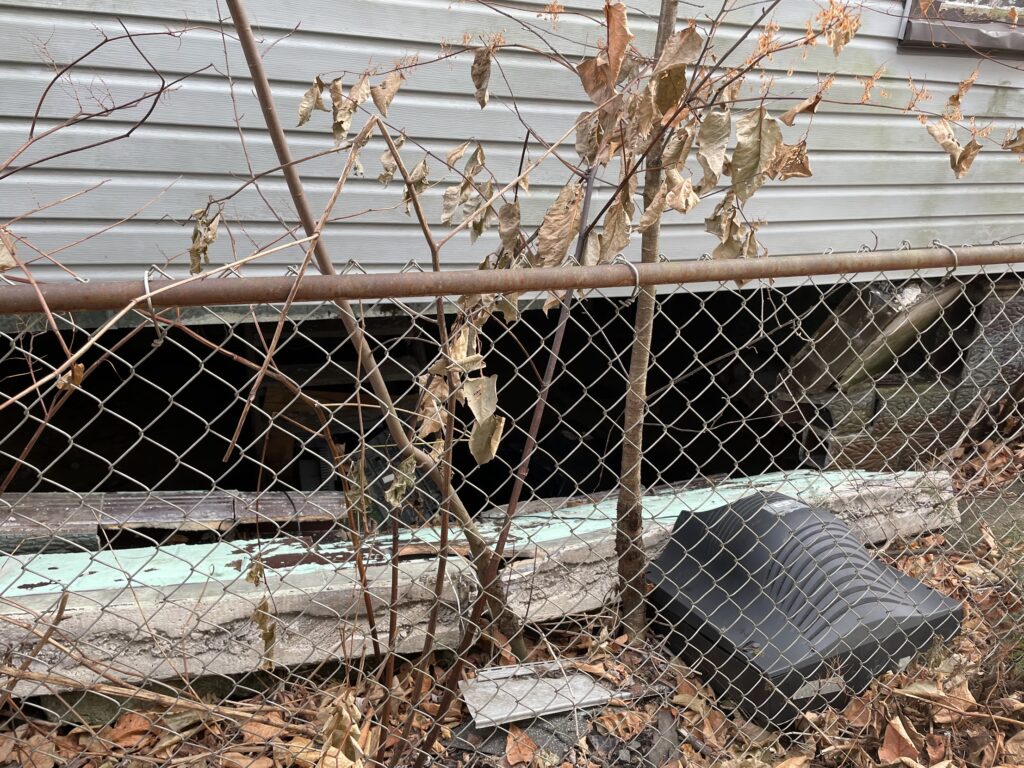 Collapsed and inward-bowed foundation wall on the right side of a duplex, exposing the basement and showing structural failure requiring full foundation replacement.