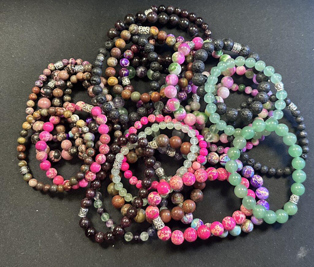 Assorted handmade natural stone bracelets stacked together showing variation in color, texture, and gemstone composition